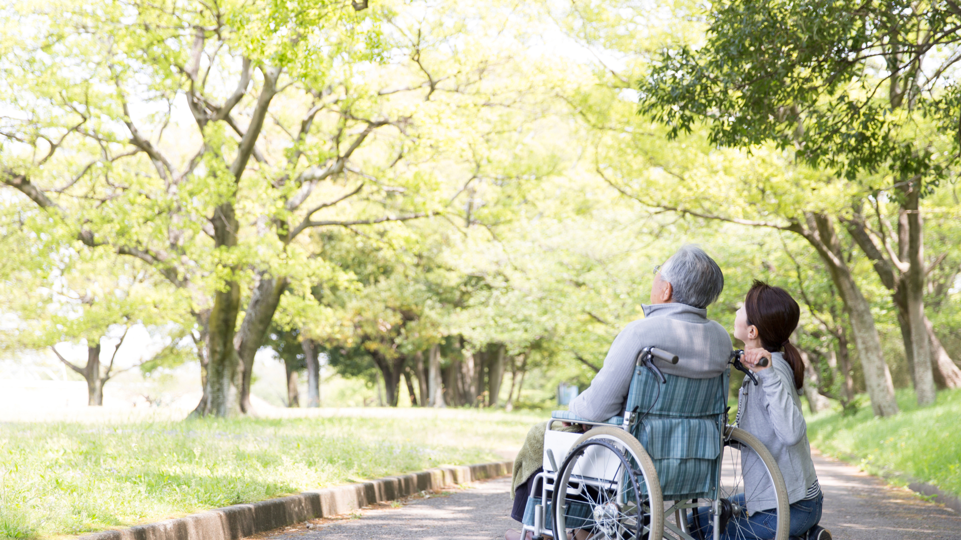 林道で空を見上げている車椅子に座っている高齢者男性と訪問看護師